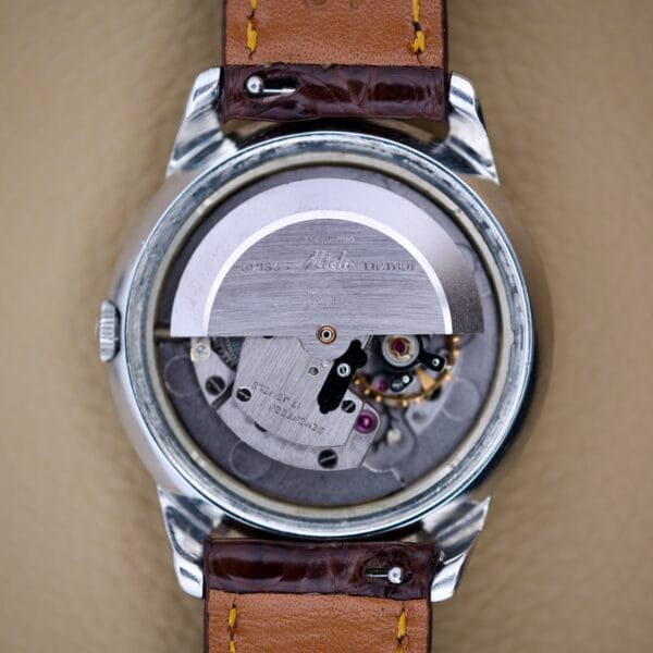 Close-up of the Mido Multifort Powerwind White Dial, showcasing its exposed Automatic Cal. 917P movement with visible gears and metal parts, paired with a brown leather strap.