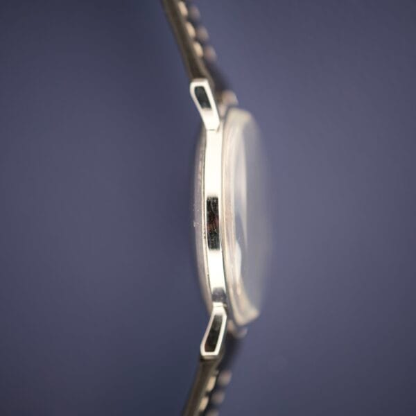 Side view of the Hamilton Accumatic X Sunburst Dial Stainless Steel Cal. 667 wristwatch, featuring a stainless steel band and sunburst dial, set against a plain dark blue background.