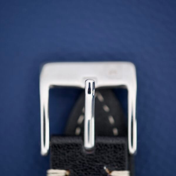 Close-up of the Hamilton Accumatic X Sunburst Dial Stainless Steel Cal. 667, featuring a shiny stainless steel buckle on a black leather strap with white stitching, set against a blue background.