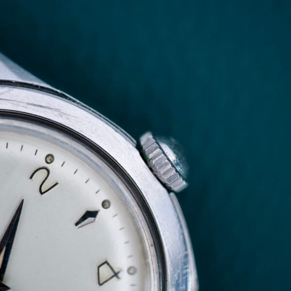 Close-up of a 1955 Bulova Automatic Stainless Steel Cal. 11ACAC watch, highlighting its crown, partial watch face with Arabic numerals, and stainless steel case.