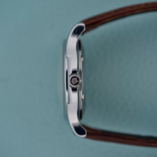 Side view of the Hamilton Automatic Date Ref. 6239, a stainless steel wristwatch with 25 jewels and a brown leather strap, set against a light blue background.