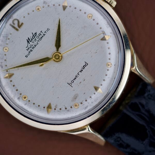 Close-up of a vintage Mido Multifort Super Automatic Powerwind 14k Gold Capped Cal. 917R wristwatch with a black leather strap.