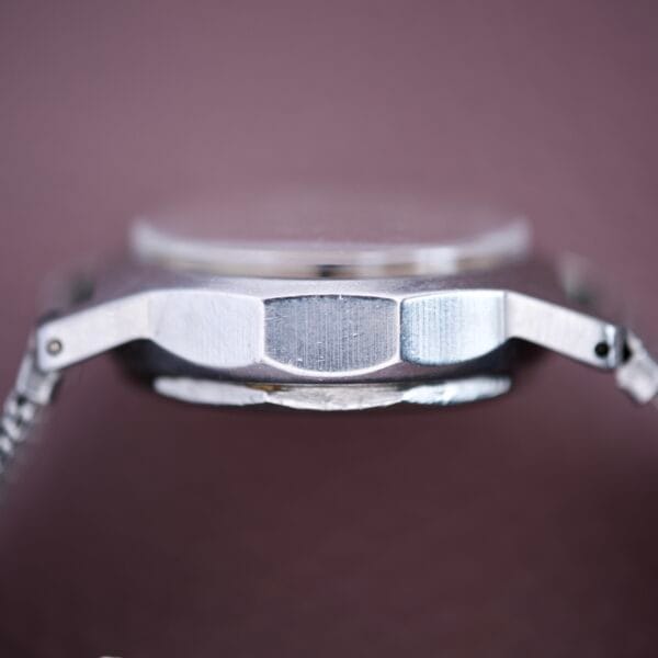 Close-up side view of the Mido Multifort Super Automatic Bumper with stainless steel case, showcased against a blurred mauve background.