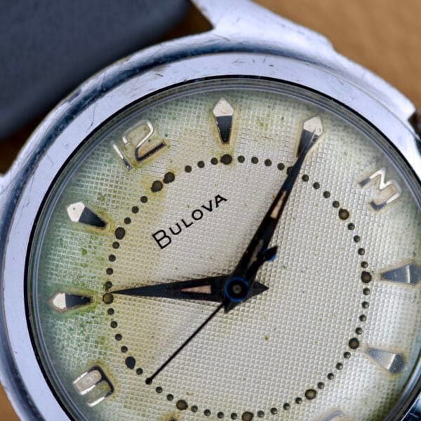 Close-up of a Bulova Waffle Dial Manual Wind Cal. 11ACC, US Zone Germany, showing 2:07 on its worn and slightly discolored waffle-patterned dial.