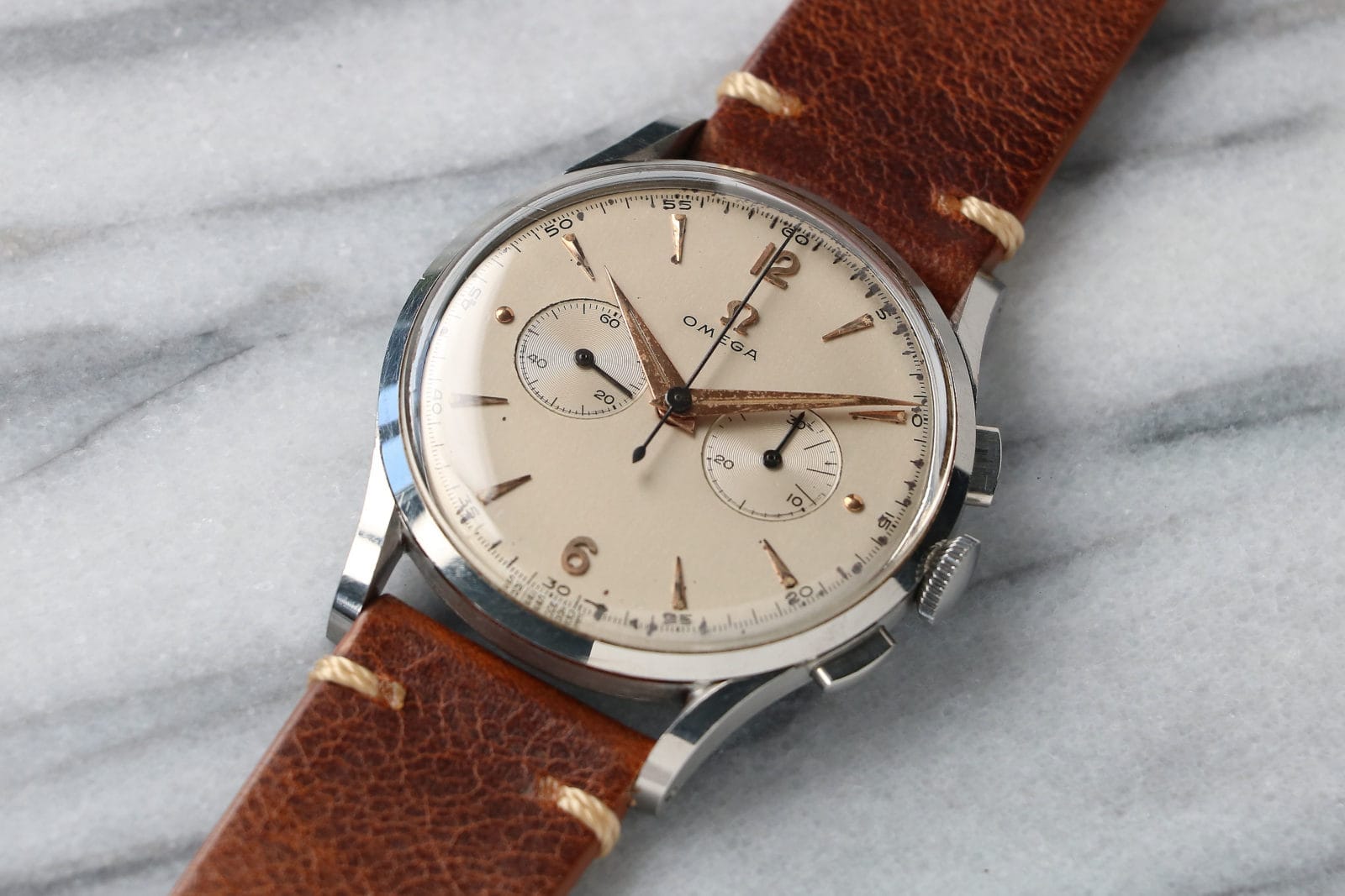 A vintage Omega wristwatch with a brown leather strap rests elegantly on a marble surface, perfect for collectors or those browsing eBay for timeless style.