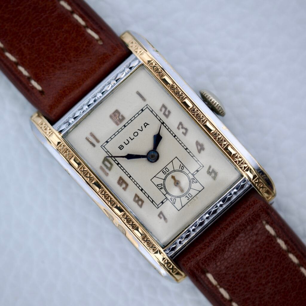 The 1929 Bulova President Art Deco Tank wristwatch features a rectangular gold-tone case, 17 Jewels Cal. 9AF movement, and a brown leather strap, showcased against a white background.