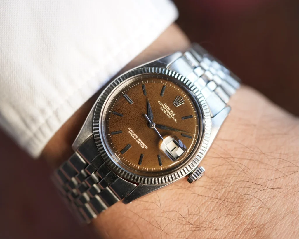 A brown-dial Rolex Datejust watch with a metal strap worn on a person’s wrist in a white shirt.