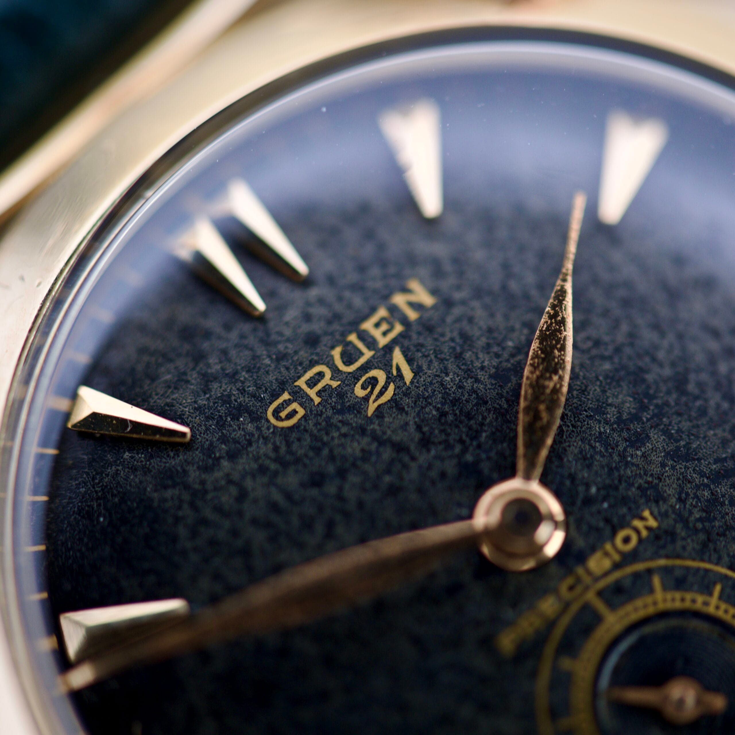 The Rise and Fall of American Watchmaking: A Complete History 1 Close-up of a vintage Gruen 21 wristwatch, a fine example of American watchmaking, with gold hands and markers on a textured dark blue dial.