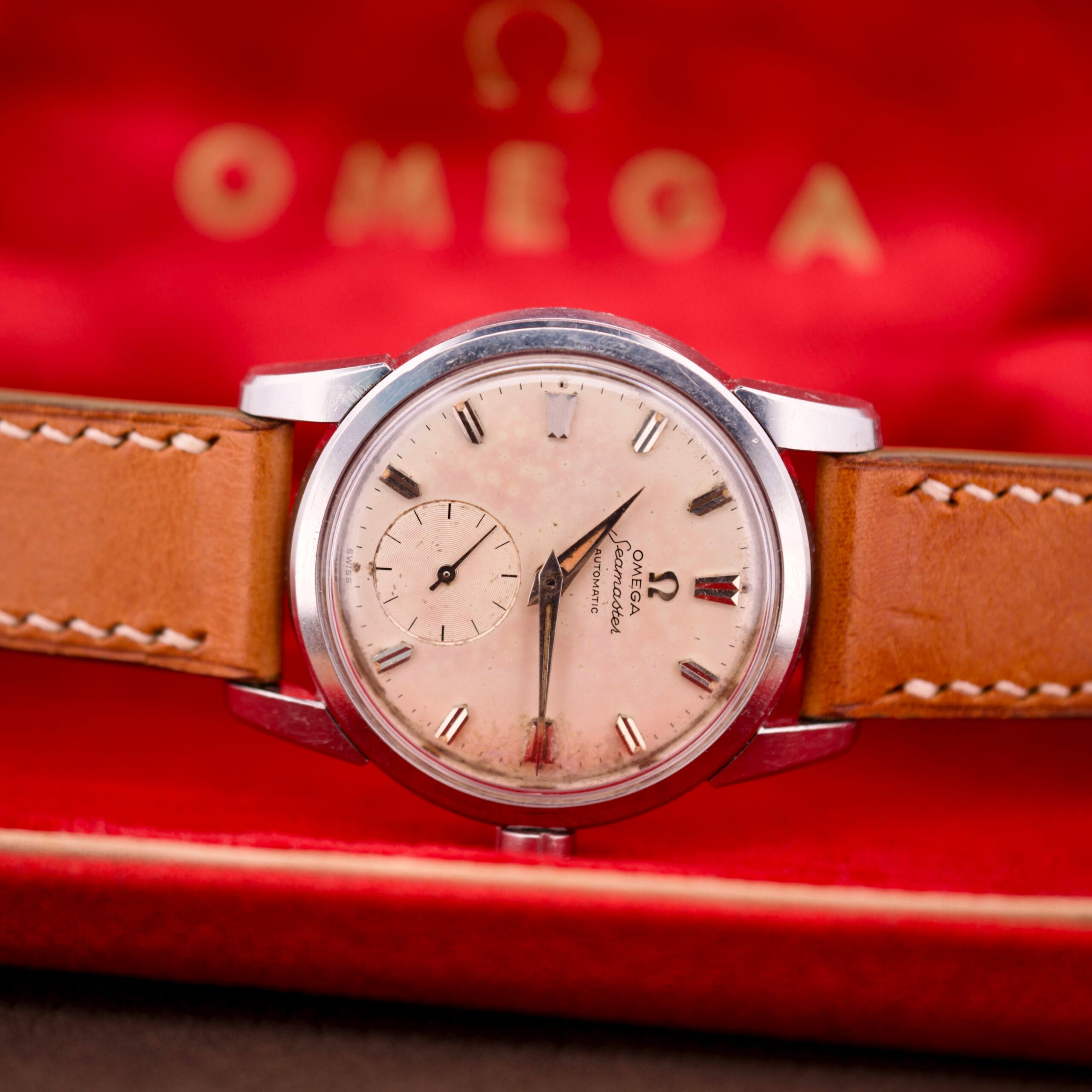 A vintage Omega Seamasters wristwatch with a tan leather strap, elegantly presented in a red Omega box.