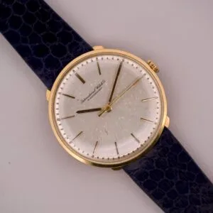 The IWC "Stubby Lugs" Calatrava 18k Yellow Gold Cal. 401 features a white dial with black hands, distinctive stubby lugs, and a dark textured leather strap—a classic design shown against a light background.