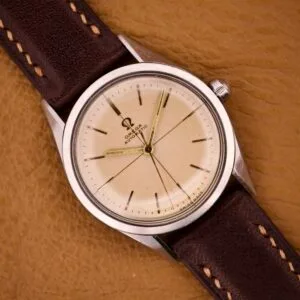 An Omega Automatic Ref. 2802-1 with cross hair cream dial, Cal. 471 movement, and brown leather strap is displayed on a tan surface.