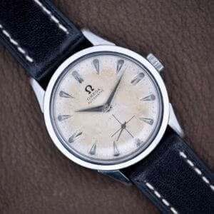 Top-down view of vintage Omega Automatic FX 6040 on black leather strap, cream-patina dial and sharp steel case.