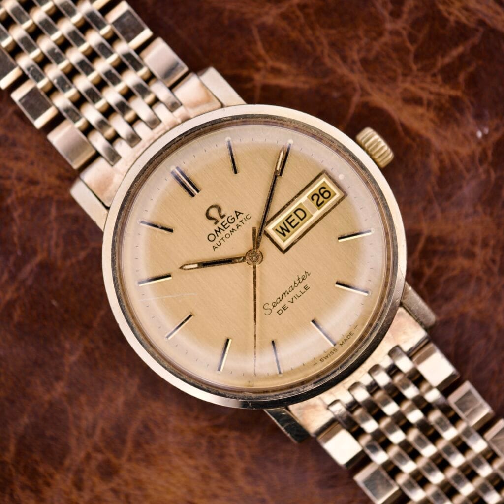 An Omega Seamaster Deville Day/Date Ref. 166.0209 Cal. 1020 watch featuring a day/date display, presented on a brown leather background.
