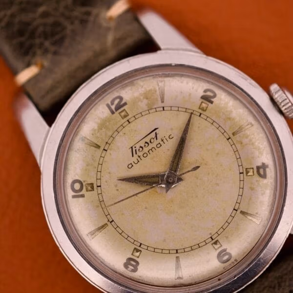 Tissot Ref. 6590 dial close-up at 3/4 angle showing applied steel Arabic numerals at the even hours with polished wedge markers at the odd positions.