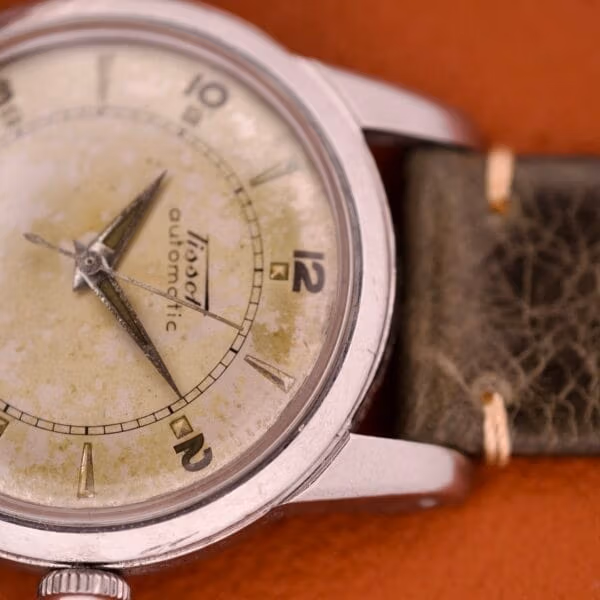 Macro detail of the cursive Tissot logo and italic automatic script across the heavily patinated cream and olive 6590 dial.