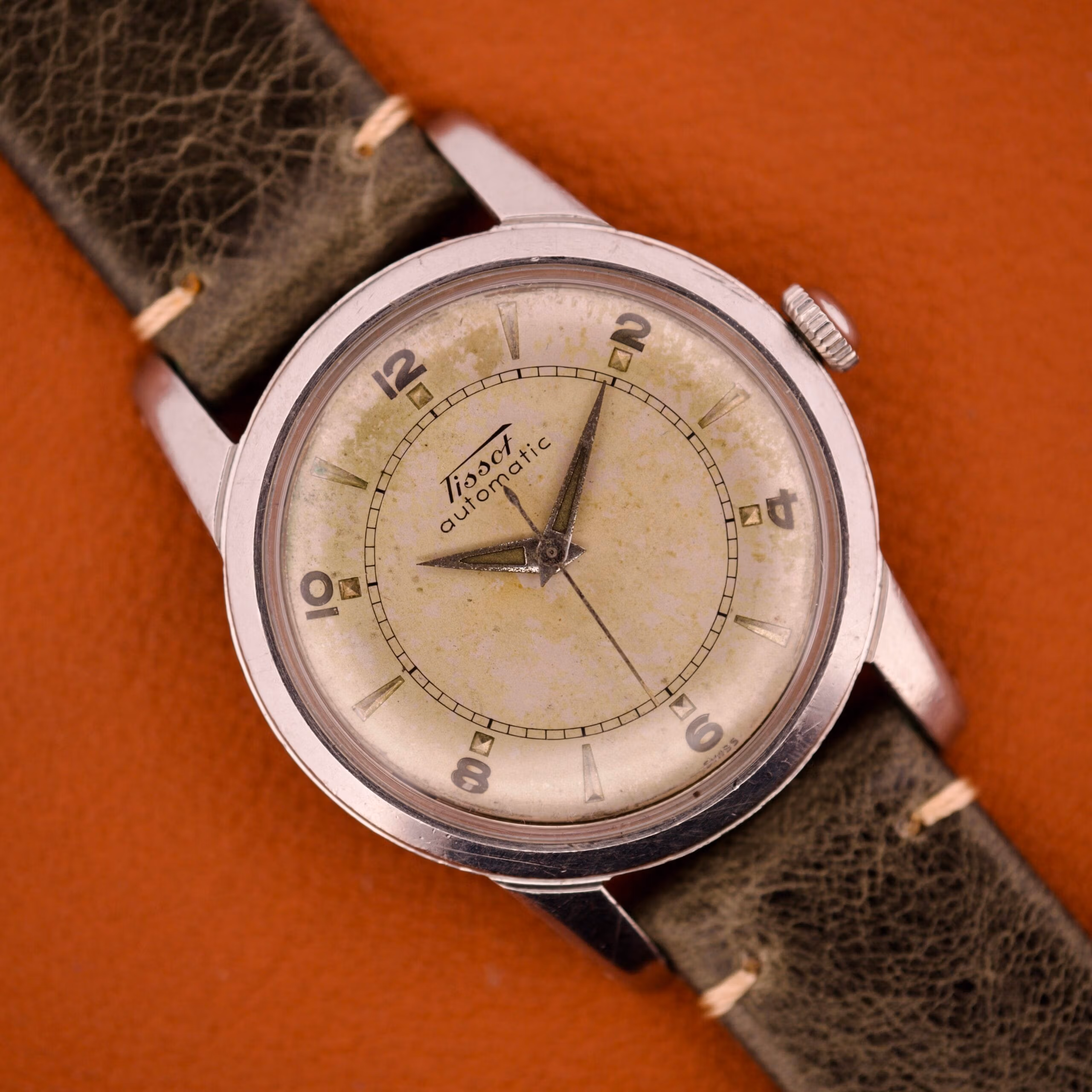 Front of vintage Tissot Automatic Bumper Ref. 6590 in stainless steel showing the heavily mottled cream and olive tropical silver dial with dauphine hands.