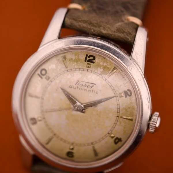 Front 3/4 wrist-angle of the Tissot 6590 with the signed crown and the heavily aged tropical dial showing cream, yellow, and olive zones.