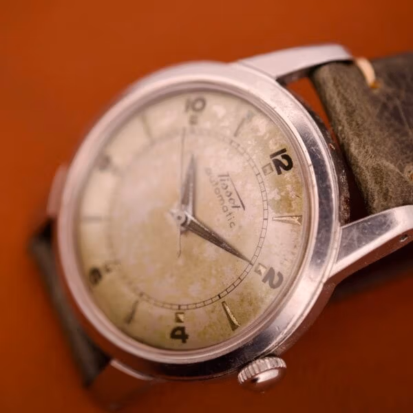 Top-down 3/4 view of the Tissot Automatic Bumper Ref. 6590 with signed crown at 3 and dauphine hands across the tropical silver dial.