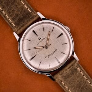 The Hamilton Thin-O-Matic Linen Dial Micro Rotor Cal. 663 wristwatch is shown with a brown leather strap, displayed on a matching brown surface.