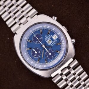 An Omega Seamaster Speedsonic F300 Ref. 188.0002 chronograph with original bracelet and Spanish date display, featuring a silver case and blue dial, rests elegantly on a brown surface.