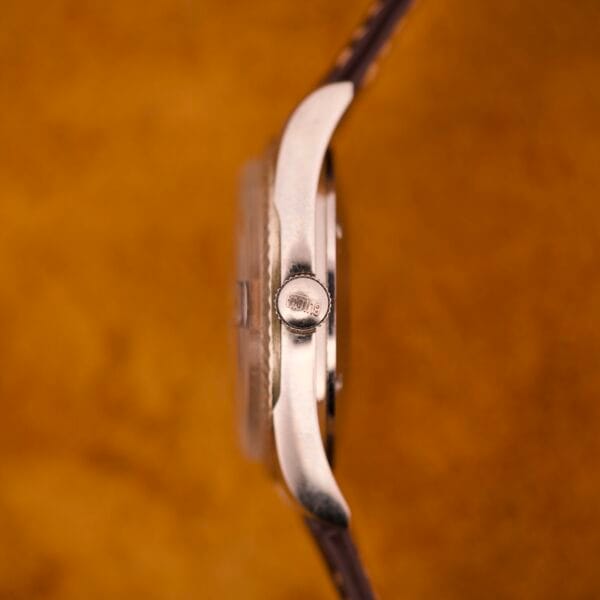 Side view of the Bulova Oceanographer Automatic Date Black Dial Fluted Bezel watch with a brown strap, set against a textured orange background.