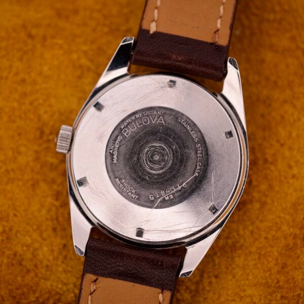 Close-up of the back of a Bulova Oceanographer Automatic Date Black Dial Fluted Bezel wristwatch with a brown leather strap on a yellow surface.