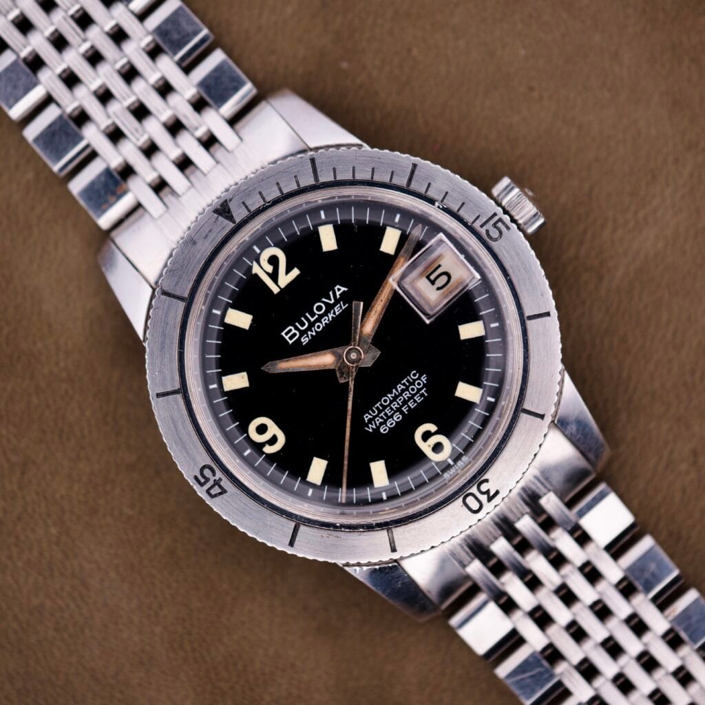 Close-up of a Bulova Snorkel Automatic Devil Diver Ref. 386 with black dial and silver metal band, displayed on a brown surface.