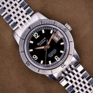 Close-up of a Bulova Snorkel Automatic Devil Diver Ref. 386 with black dial and silver metal band, displayed on a brown surface.