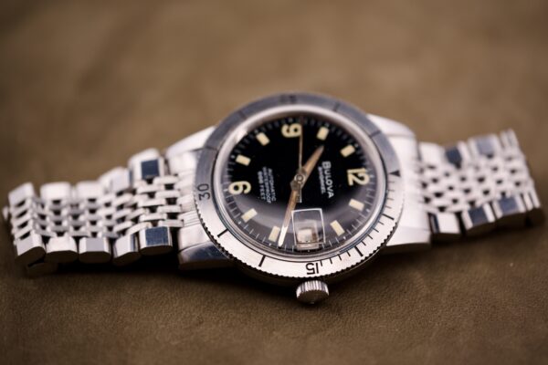 A Bulova Snorkel Automatic Devil Diver Ref. 386 with black dial and metal band rests on a brown surface.