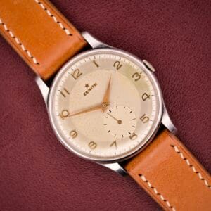 A Zenith Caltrava Jumbo wristwatch with a stainless steel case, Arabic numerals, and subseconds sits on a textured brown surface.