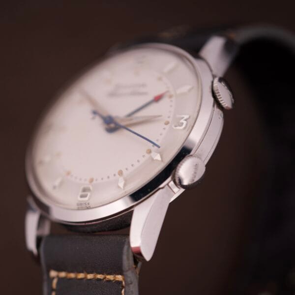 Close-up of a NOS Bulova Wrist Alarm Manual Wind Cal. 11AERC, featuring a white dial, blue hands, and a black leather strap with tan stitching.