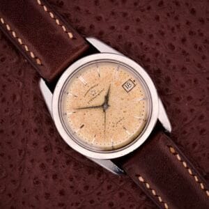 An Eterna-Matic Chronometer Automatic Date 21 Jewels wristwatch with a tropic dial and brown leather strap rests on a textured brown surface.