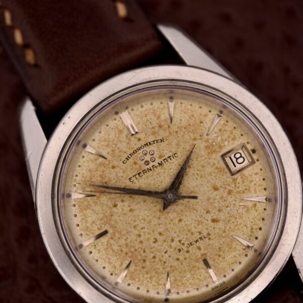 The Eterna-Matic Chronometer Automatic Date Tropic Dial 21 Jewels features a speckled cream tropic dial, automatic date function, and comes with a brown leather strap.