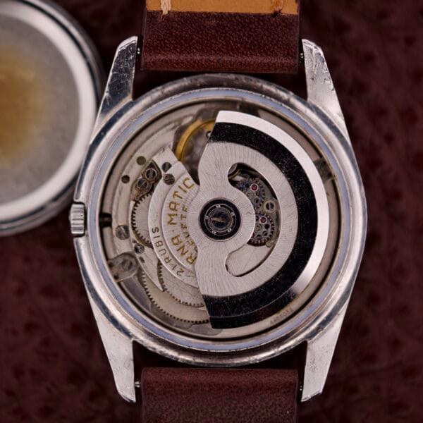 Close-up of an open Eterna-Matic Chronometer Automatic Date Tropic Dial 21 Jewels wristwatch, revealing its mechanical movement and gears, with a brown leather strap.
