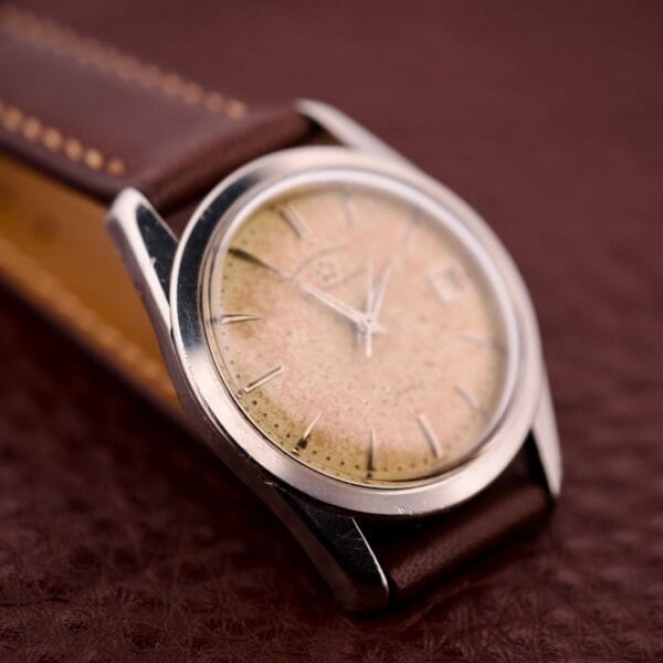 An Eterna-Matic Chronometer Automatic Date Tropic Dial 21 Jewels wristwatch with a brown leather strap is displayed on a textured brown surface.