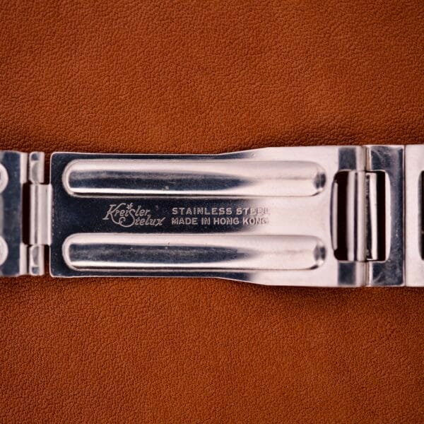 Close-up of a Bulova Day/Date 23 Jewels Automatic Two Tone Cushion Case Fluted Bezel metal clasp engraved with Stainless Steel, Made in Hong Kong, resting on a brown surface.