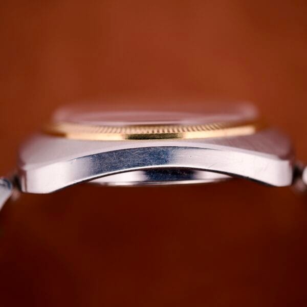 Close-up side view of the Bulova Day/Date 23 Jewels Automatic, showcasing its two tone cushion case and fluted bezel, set against a brown background.