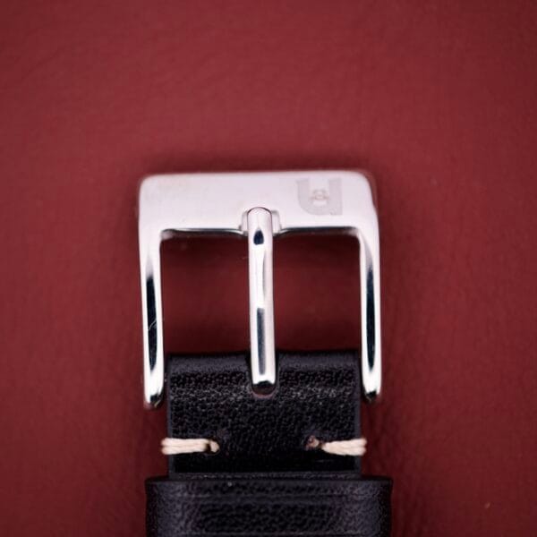 A close-up of the Universal Geneve Quartz Ref. 874 108 stainless steel cushion case with a black leather strap, set against a maroon background.