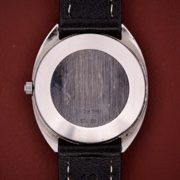 Close-up of a Universal Geneve Quartz Ref. 874 108 stainless steel cushion case wristwatch back, showing visible serial numbers against a vibrant red background.