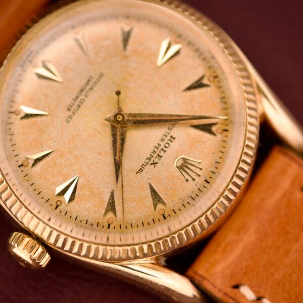 Close-up of a vintage Rolex Oyster Perpetual 'Bombay' Ref. 6593 with a 14K yellow gold case, tan leather strap, and worn dial.