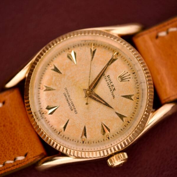 A vintage Rolex Oyster Perpetual 'Bombay' Ref. 6593 with a 14K yellow gold case, tan leather strap, and weathered cream-colored dial.