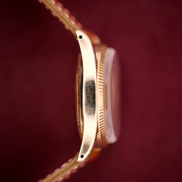 Close-up side view of a Rolex Oyster Perpetual 'Bombay' Reference 6593 with a 14K yellow gold case, set against a dark red background.