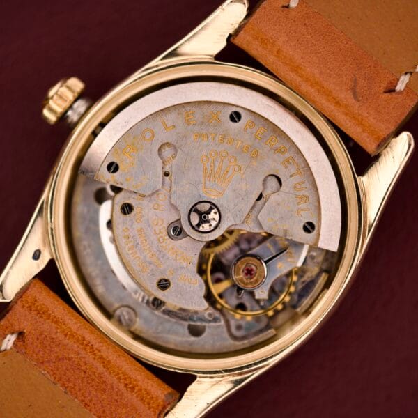 Close-up of the Rolex Oyster Perpetual 'Bombay' Ref. 6593 with visible gears and a tan leather strap, highlighting its classic 14K yellow gold case and timeless craftsmanship.