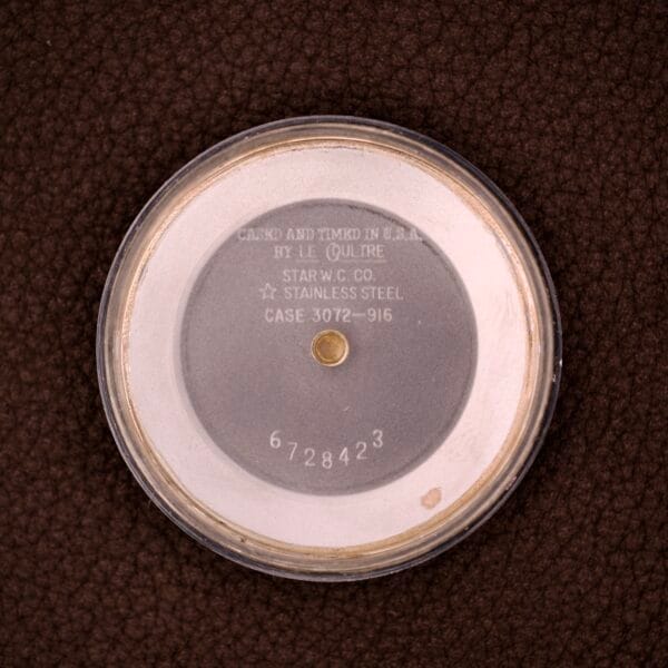 Round stainless steel case back sits on a brown textured surface, with engraved details—highlighting the precision of the Lecoultre Automatic Memovox Reveil "Egg" Ref. 3072-916 Cal. 916.