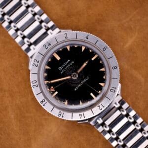 Bulova Accutron Astronaut 214 GMT 24 Hour Bezel Black Dial wristwatch with metal band, displayed on a brown surface.