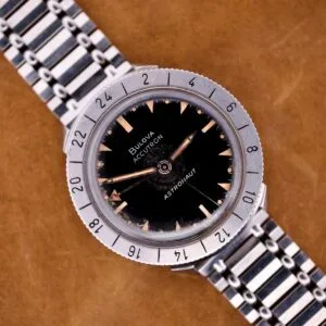 Bulova Accutron Astronaut 214 GMT 24 Hour Bezel Black Dial wristwatch with metal band, displayed on a brown surface.