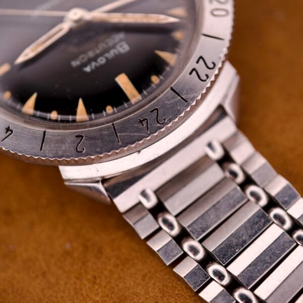 Close-up of the Bulova Accutron Astronaut 214 GMT 24 Hour Bezel Black Dial watch featuring a metal bracelet, black dial, numerals, hour markers, and signature GMT bezel.