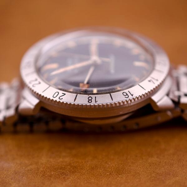 Close-up of a Bulova Accutron Astronaut 214 GMT with a 24 Hour Bezel and black dial, displayed on a brown surface.
