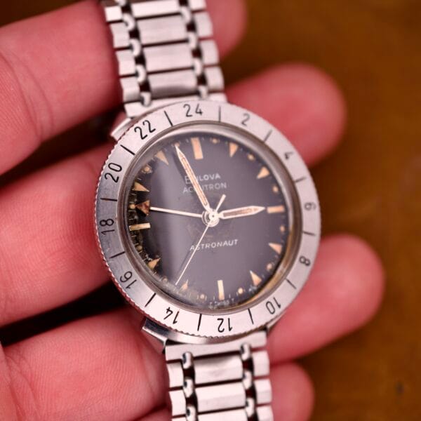 A hand holding a Bulova Accutron Astronaut 214 GMT with 24 Hour bezel and black dial.