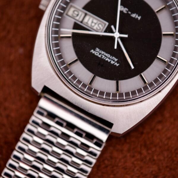 Close-up of a Hamilton Automatic HF-36 Day-Date Hi-Beat Cal. 631 wristwatch with a metal mesh band on a brown textured surface.